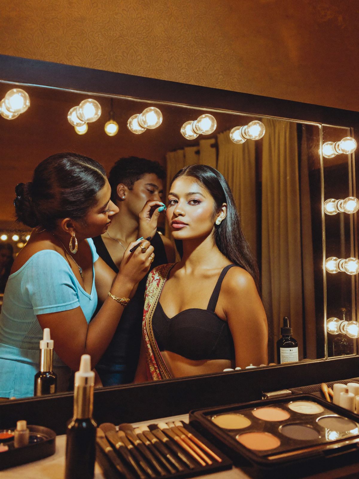 A make-up artist preparing a model at a lit mirror